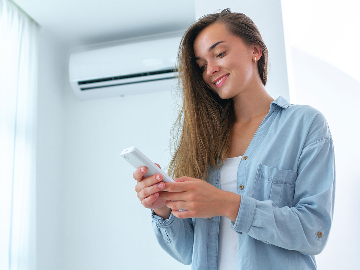 female holding air conditioner remote while standing underneath it