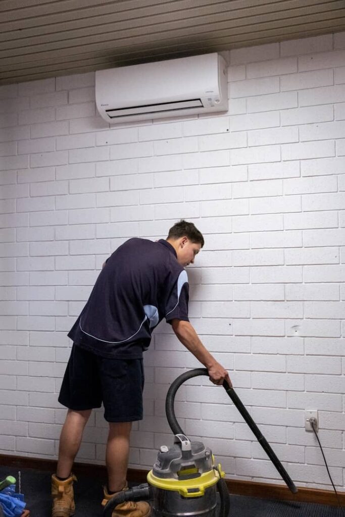 Technician cleaning beneath a wall mounted split system air conditioner indoor unit during a Perth air conditioning service.